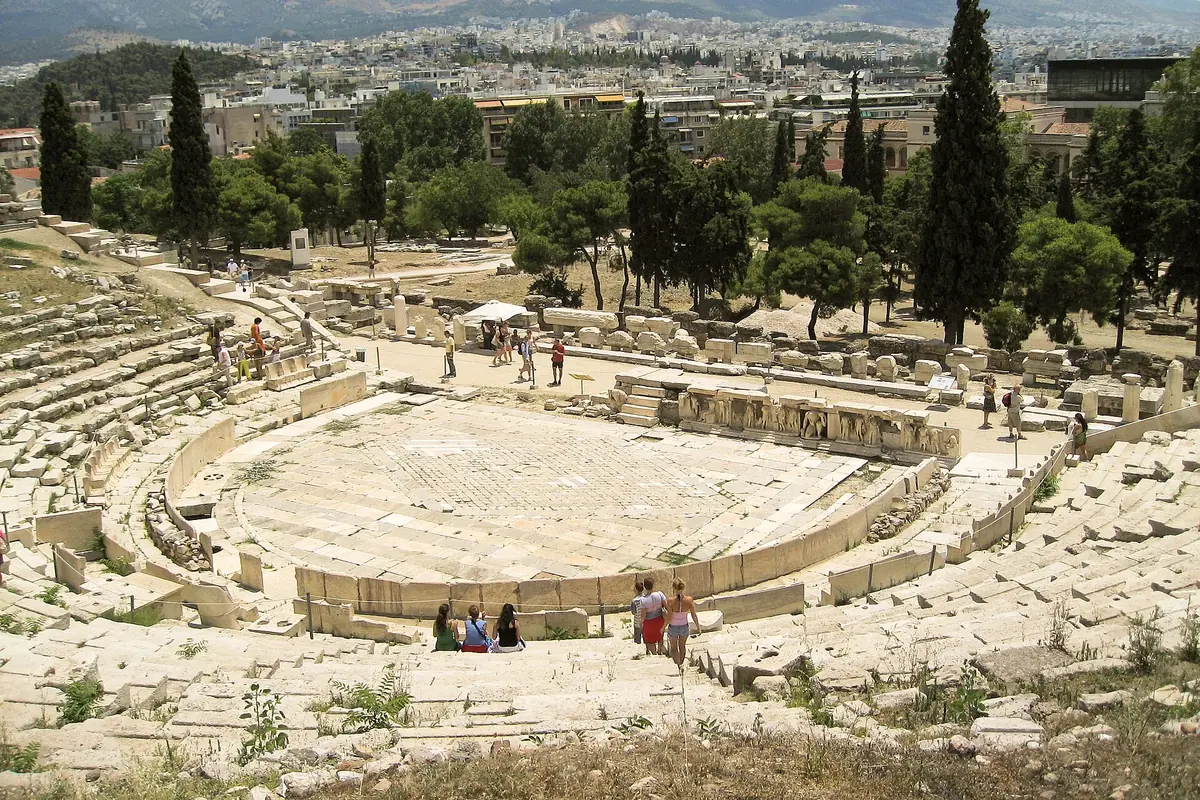 The stone seating and circular floor of the Theatre of Dionysus on the south slope of the Acropolis, with the city beyond.