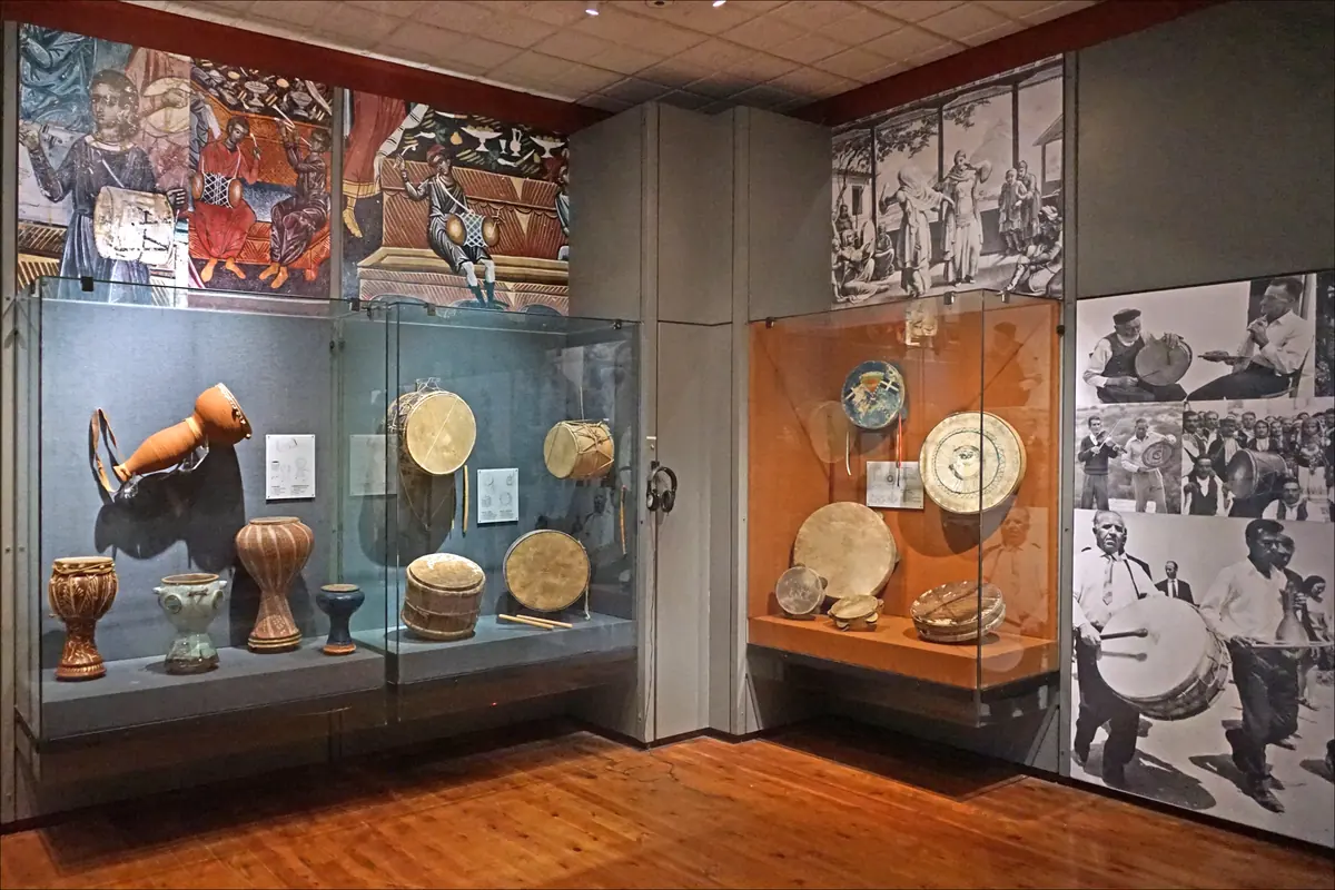 A museum room with glass cases of Greek folk drums and tambourines and wall photographs of dancers and drummers